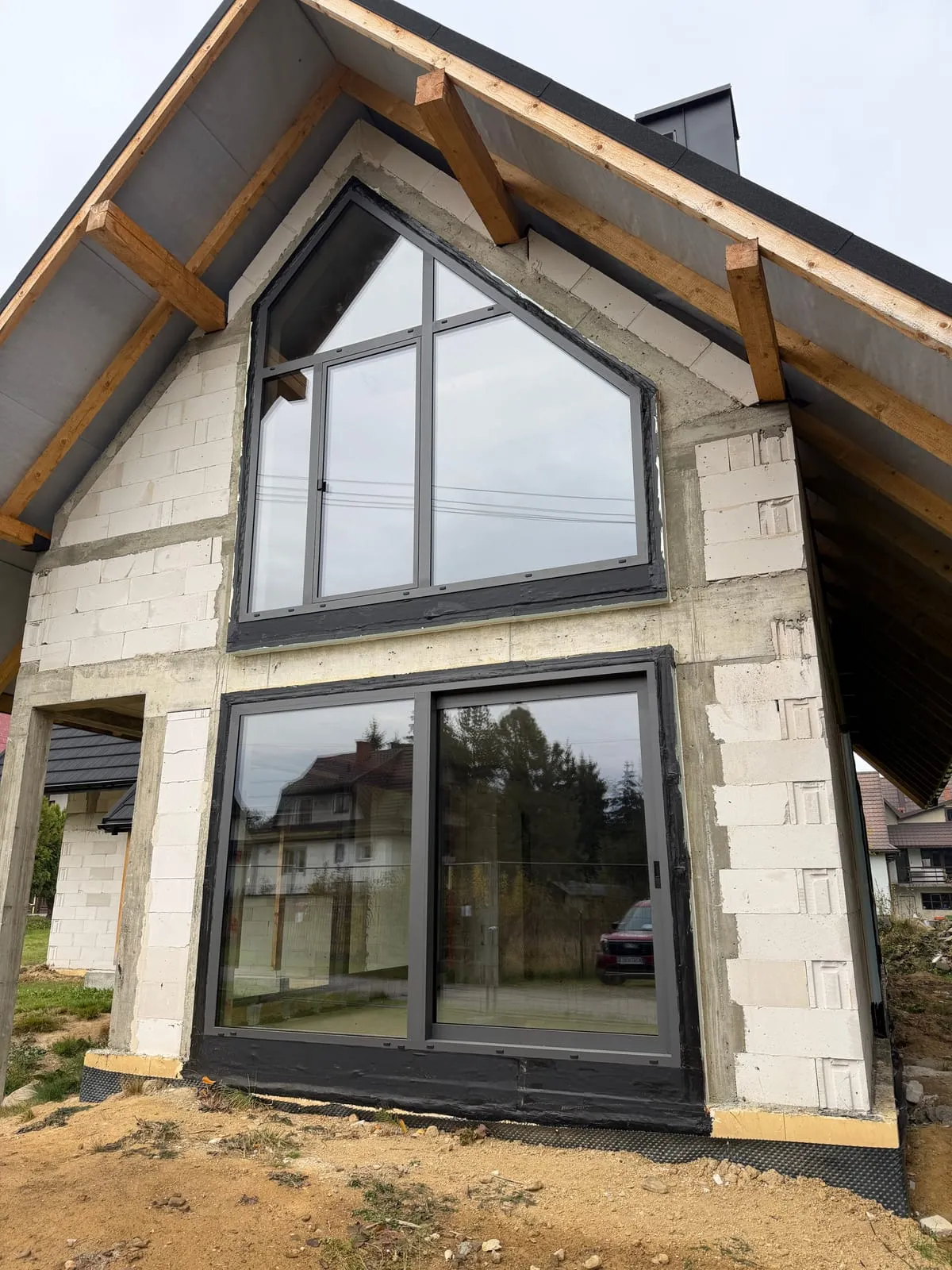Szczyt domu od frontu, aluminiowa witryna ze skosami nad drzwiami przesuwnymi HST, stolarka w kolorze DB703