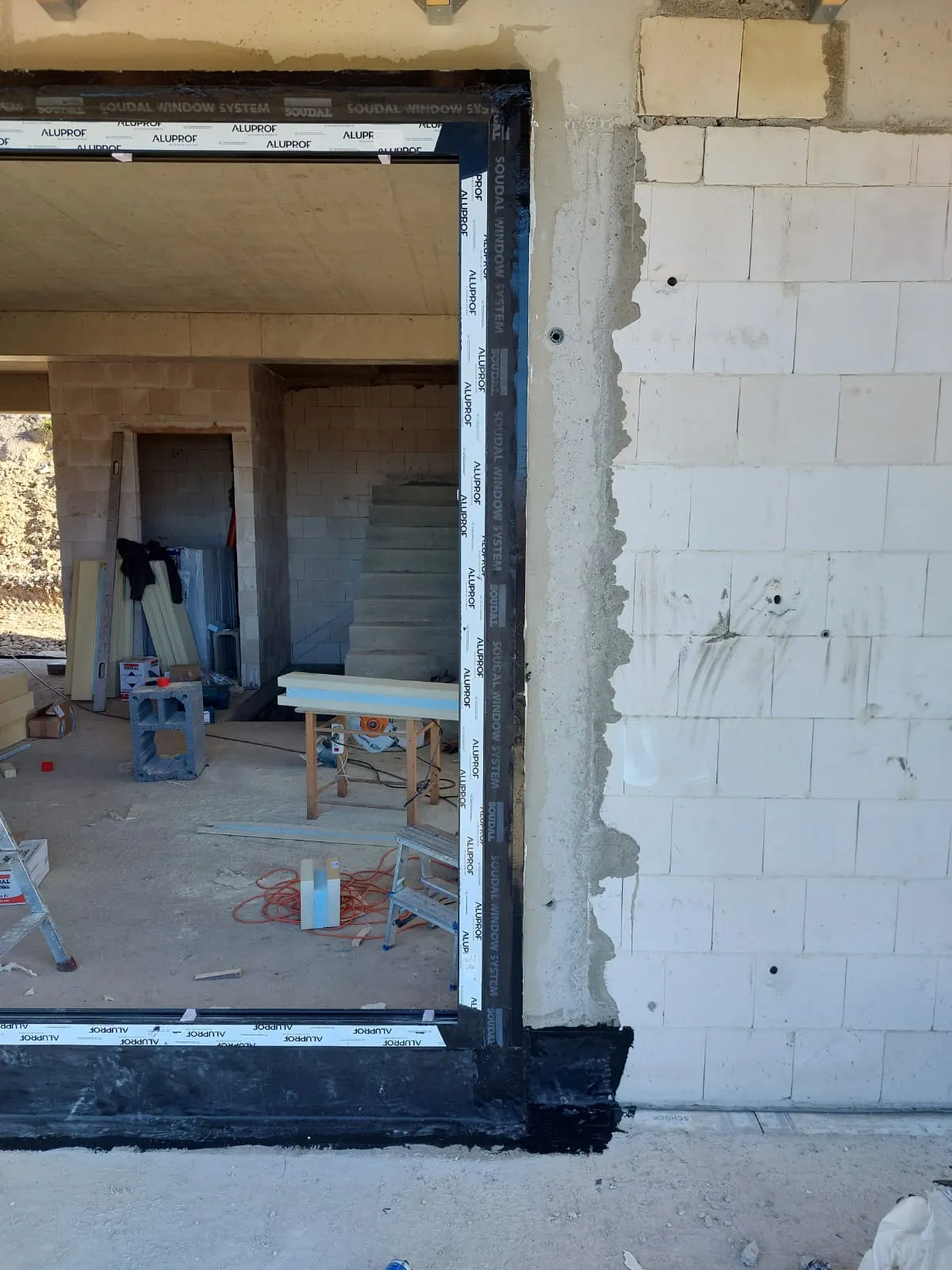 Duże okno aluminiowe osadzone na belkach Winframer, widok z wnętrza domu w stanie surowym, hydroizolacja progu