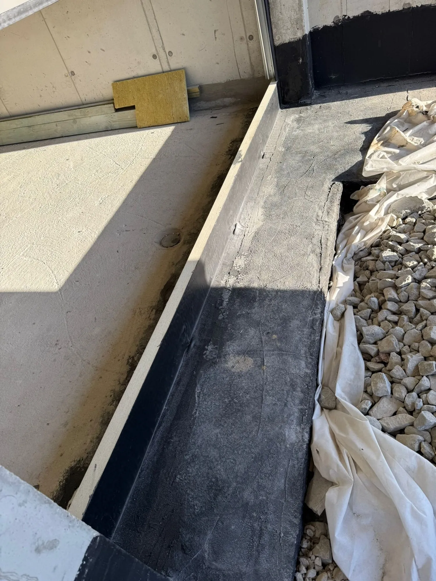 Podwalina Purenit pod bramą garażową od zewnątrz, czarna membrana EPDM połączona z hydroizolacją fundamentu, obok żwir i geowłóknina