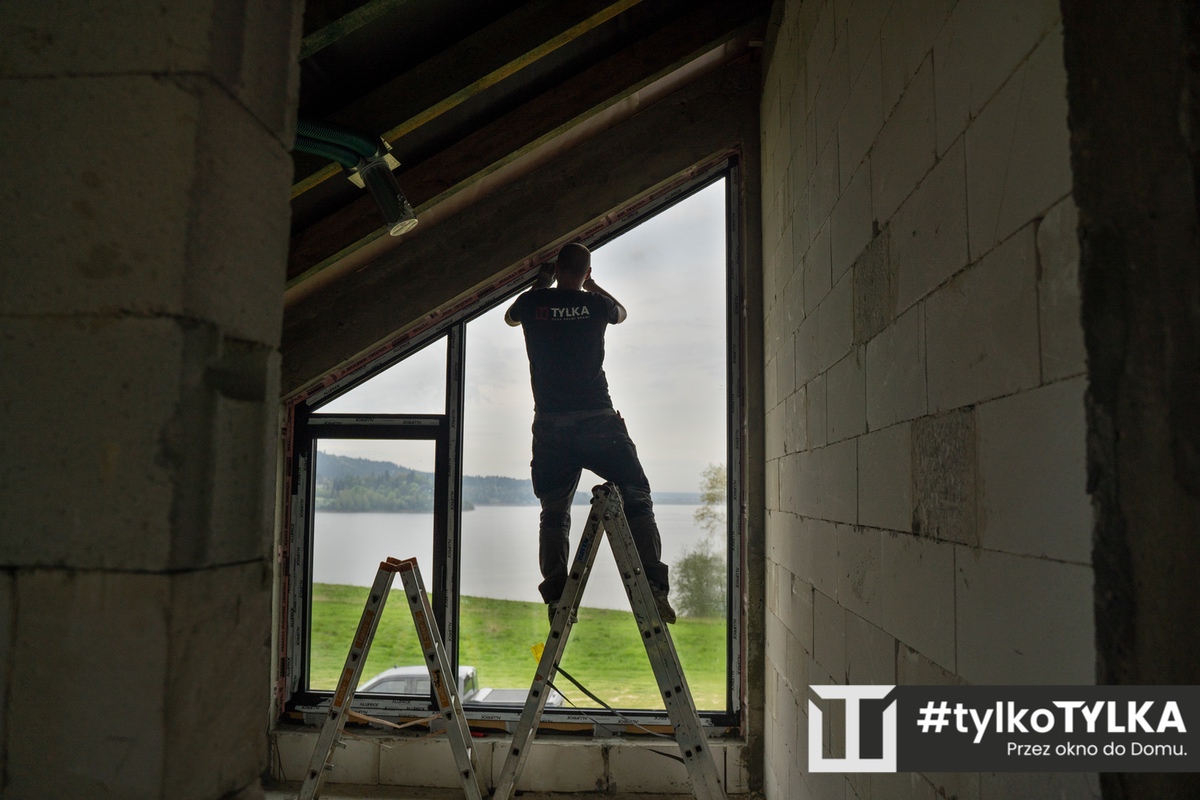 Pracownik firmy TYLKA wykleja taśmy montażowe Soudal SWS na drabince - etap montażu trójwarstwowego